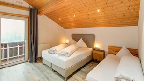 A bedroom with a wooden ceiling, a large window with curtains, a bed with white linens, and a bedside table with a lamp.