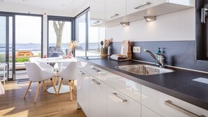 Eine moderne Küche mit großem Fenster, weißen Schränken und einer Spüle aus Edelstahl.