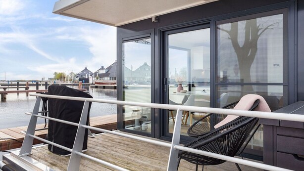 Eine moderne Terrasse mit Glastür zu einem Zimmer, einem Sessel und einem Tisch.