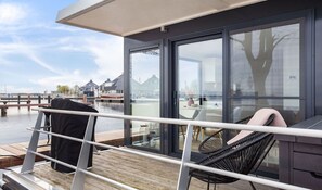A modern deck with a glass door leading to a room, a chair, and a table. - Houseboat Sneekermeer with Garden and Views (Offingawier)