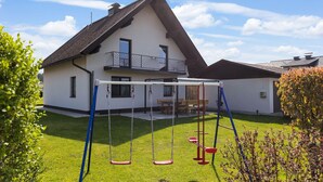 Een huis met een schuin dak, een balkon en een schommel in de tuin.