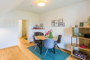 A dining area with a round table, grey chairs, and a vase with flowers. There are framed pictures on the wall and a wooden shelf with decorative items. - Apartment in Kühnsdorf near Klopeinersee (Kühnsdorf)