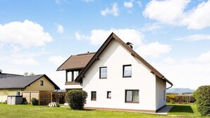 Een twee verdiepingen tellend huis met een schuin dak, een klein voortuintje en een verzorgd gazon.