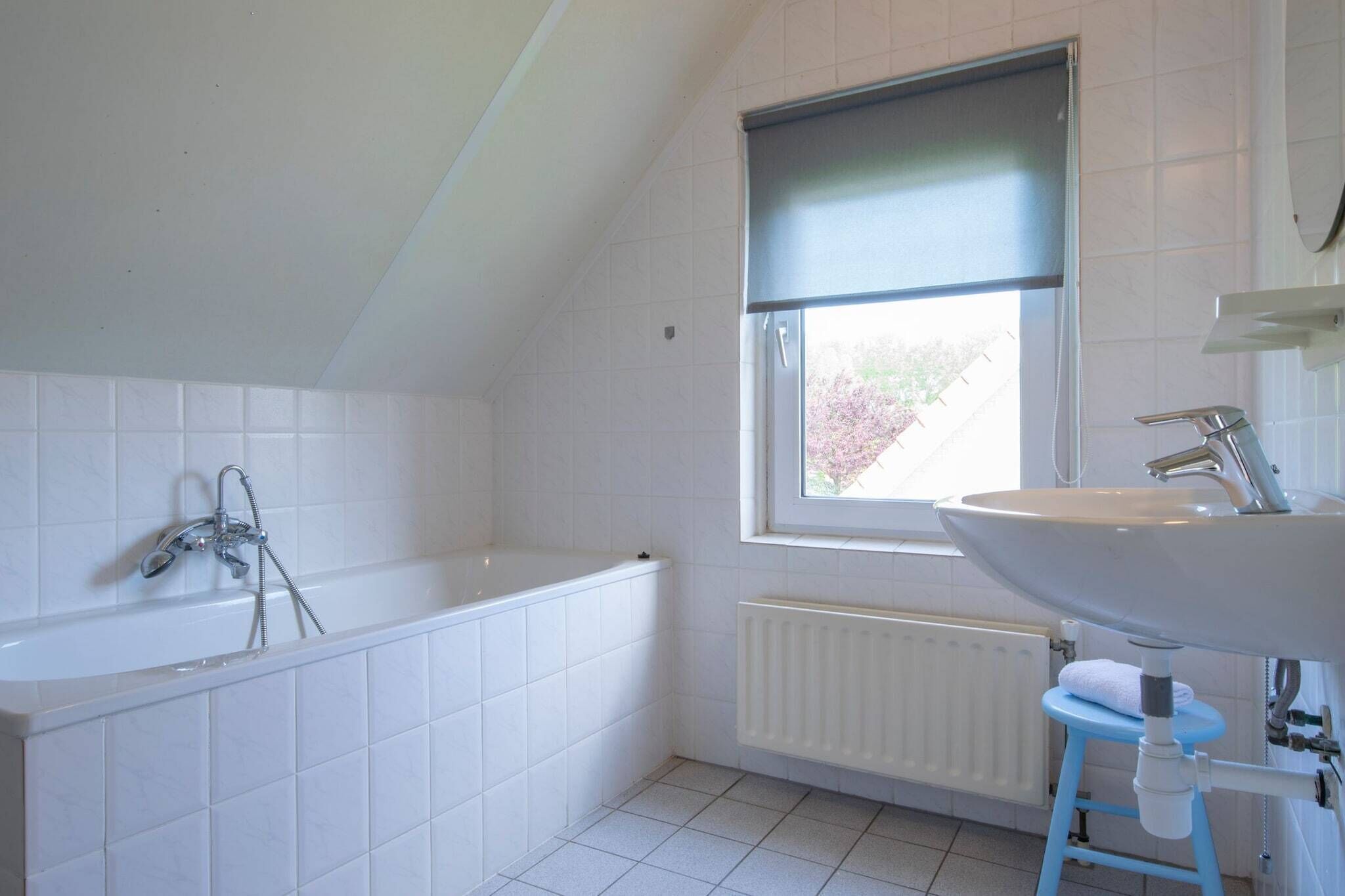 A bathroom with a bathtub, a window, a radiator, and a sink.