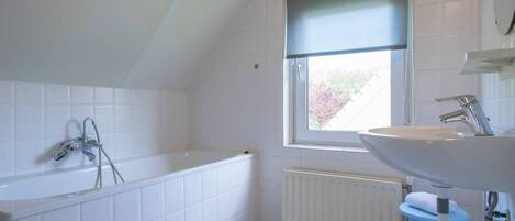 A bathroom with a bathtub, a window, a radiator, and a sink.