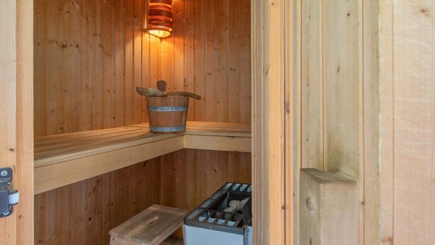 Een houten sauna met een emmer, een treeplank en een prullenbak.