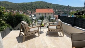 A terrace with two beige sofas and a small table, overlooking a hillside with houses and a body of water.