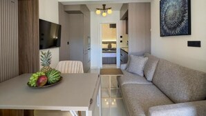 A modern living room with a sofa, a dining table with fruit, and a TV.