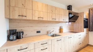 A modern kitchen with wooden cabinets, a built-in oven, and a coffee maker.