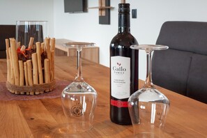 Uma mesa de madeira com uma garrafa de Gallo Family Cabernet Sauvignon 2010, dois copos de vinho e um recipiente de vidro decorativo com gravetos e flores secas.