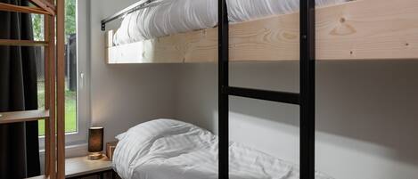 A bunk bed with white bedding, a bedside table with a lamp, and a window with curtains.