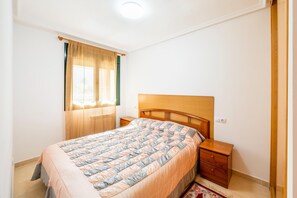 Een slaapkamer met een bed, houten hoofdbord, nachtkastjes, een raam met gordijnen en een lamp.