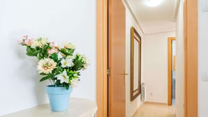 Ein Flur mit einer blauen Blumenvase auf einem weißen Schrank, Holztüren und einem gerahmten Spiegel an der Wand.