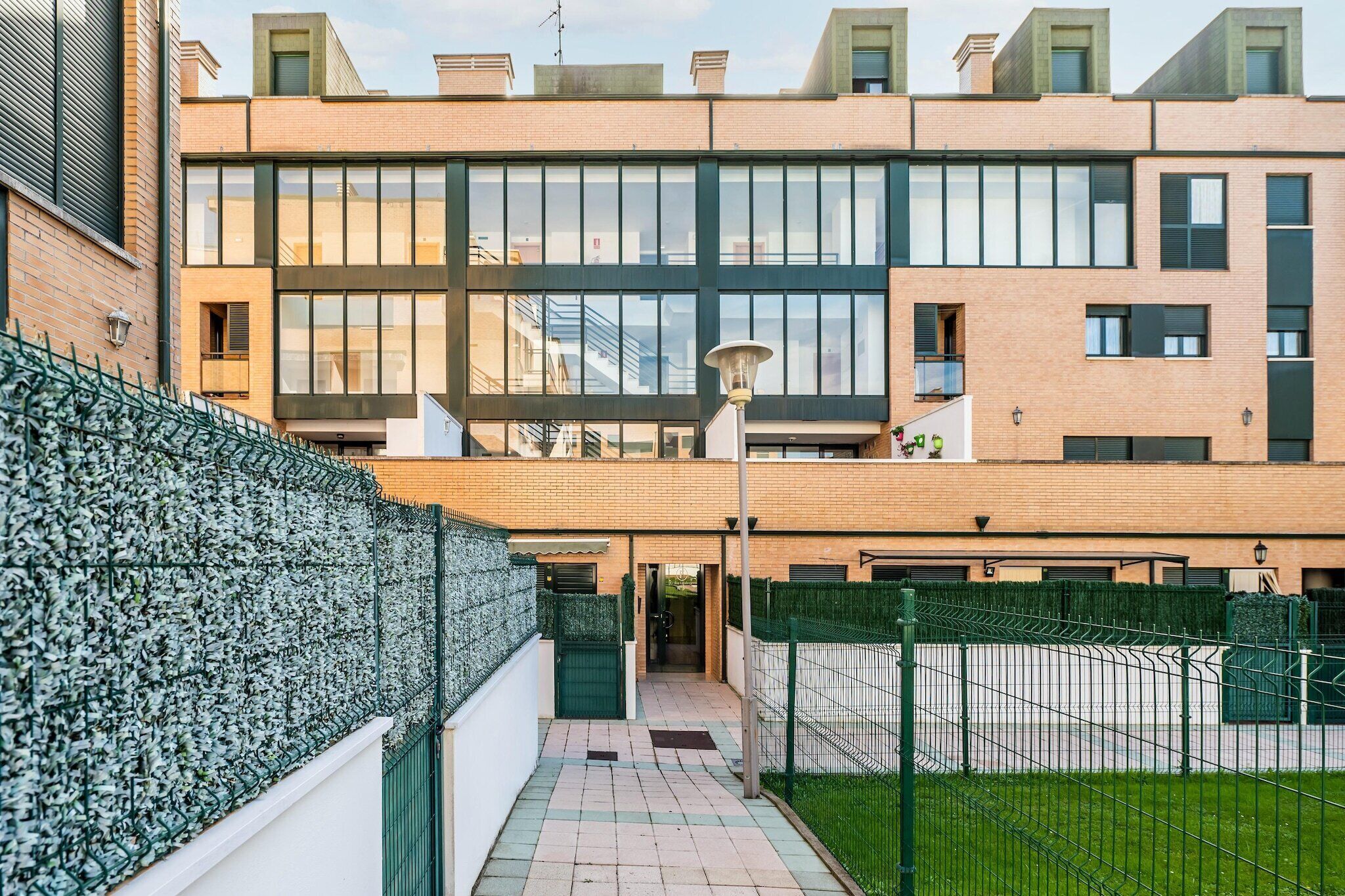 A modern building with a brick facade, large windows, and a green fence.