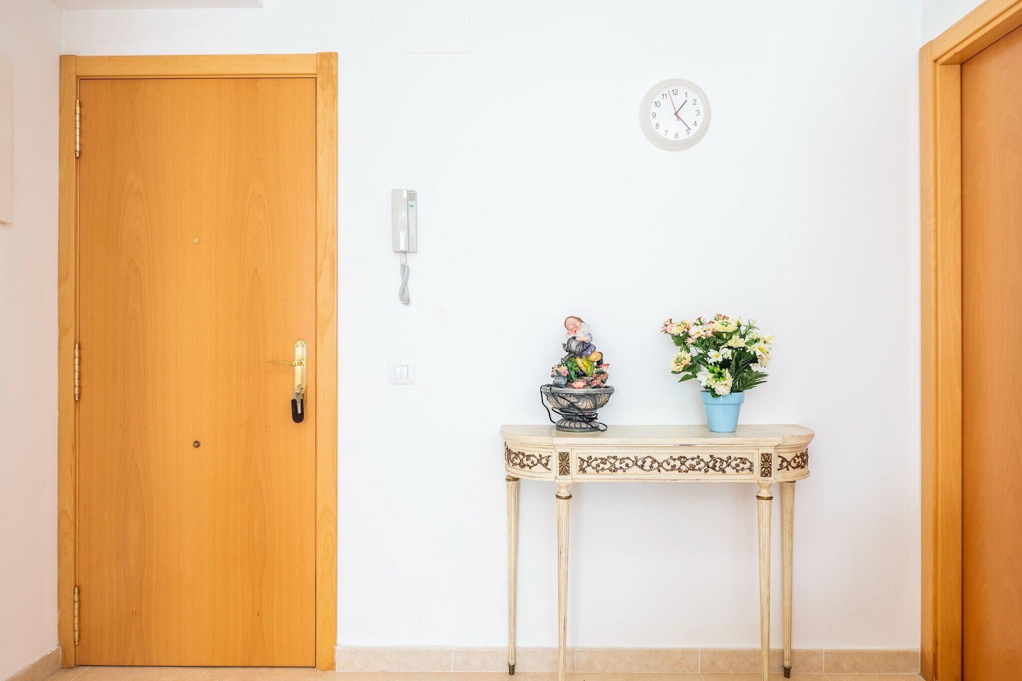 A wooden door, a wall-mounted phone, a clock, a decorative bowl, and a potted plant on a small table.