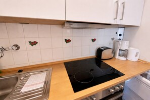 A kitchen with a black induction cooktop, a toaster, a coffee maker, and a stainless steel sink. - Appartement Elena mit Pool und Sauna (Freyung)