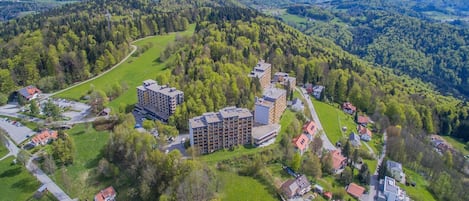 An aerial view of a residential area with a mix of single-family homes and multi-story buildings, surrounded by lush greenery and hills in the background.