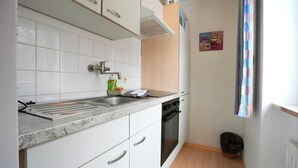 Una cocina compacta con gabinetes blancos, un lavamanos de acero inoxidable y un horno negro.
