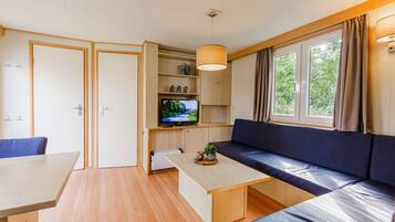 Un espacio habitable compacto con sofá, televisor, mesa de comedor y ventana con cortinas.