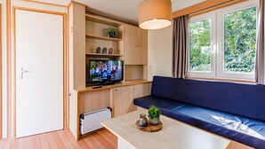 A compact living space with a television, wooden cabinets, a blue sofa, and a window with a view of greenery.