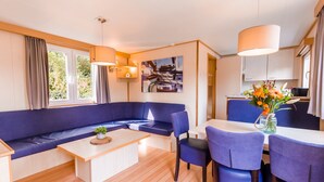 A modern living room with a blue sofa, wooden coffee table, and a dining area with blue chairs and a white table.