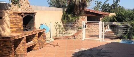 An outdoor patio with a brick barbecue grill, a gate, and a palm tree.