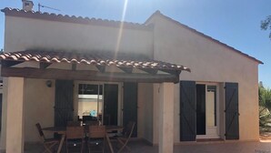 A covered patio with a table and chairs, a pergola, and a building with a tiled roof and windows. - Villa with pool (Canet-en-Roussillon)