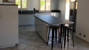 A modern kitchen with a large island, two bar stools, and a refrigerator. - Villa with pool (Canet-en-Roussillon)