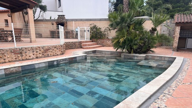 A swimming pool with a tiled deck and a stone wall. - Villa with pool (Canet-en-Roussillon)