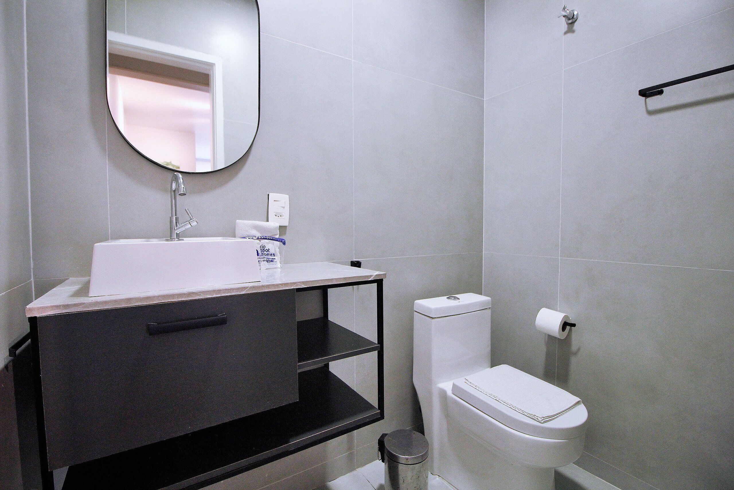 A modern bathroom with a white sink, dark vanity, and a toilet.