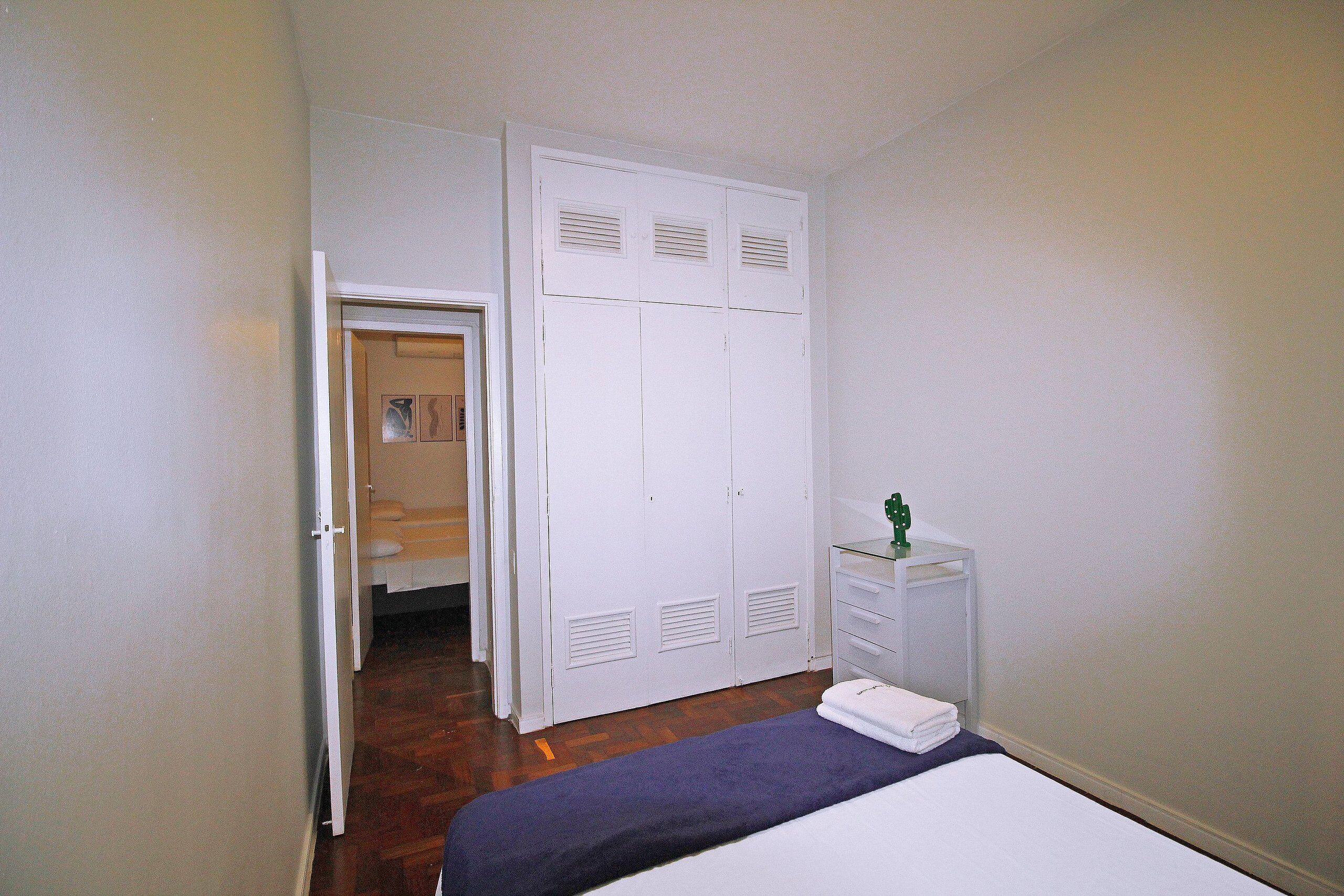 Un dormitorio con cama, un armario blanco y una mesita de noche pequeña.