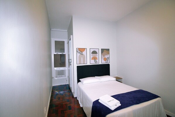 A small, neatly arranged hotel room with a single bed, a white wardrobe, and a door leading to a bathroom.