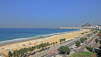 A coastal cityscape with a beach, palm-lined promenade, and a prominent mountain in the background.