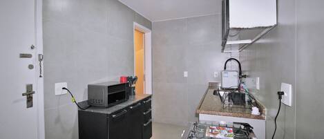 Una cocina compacta con estufa a gas, microondas y un refrigerador pequeño.
