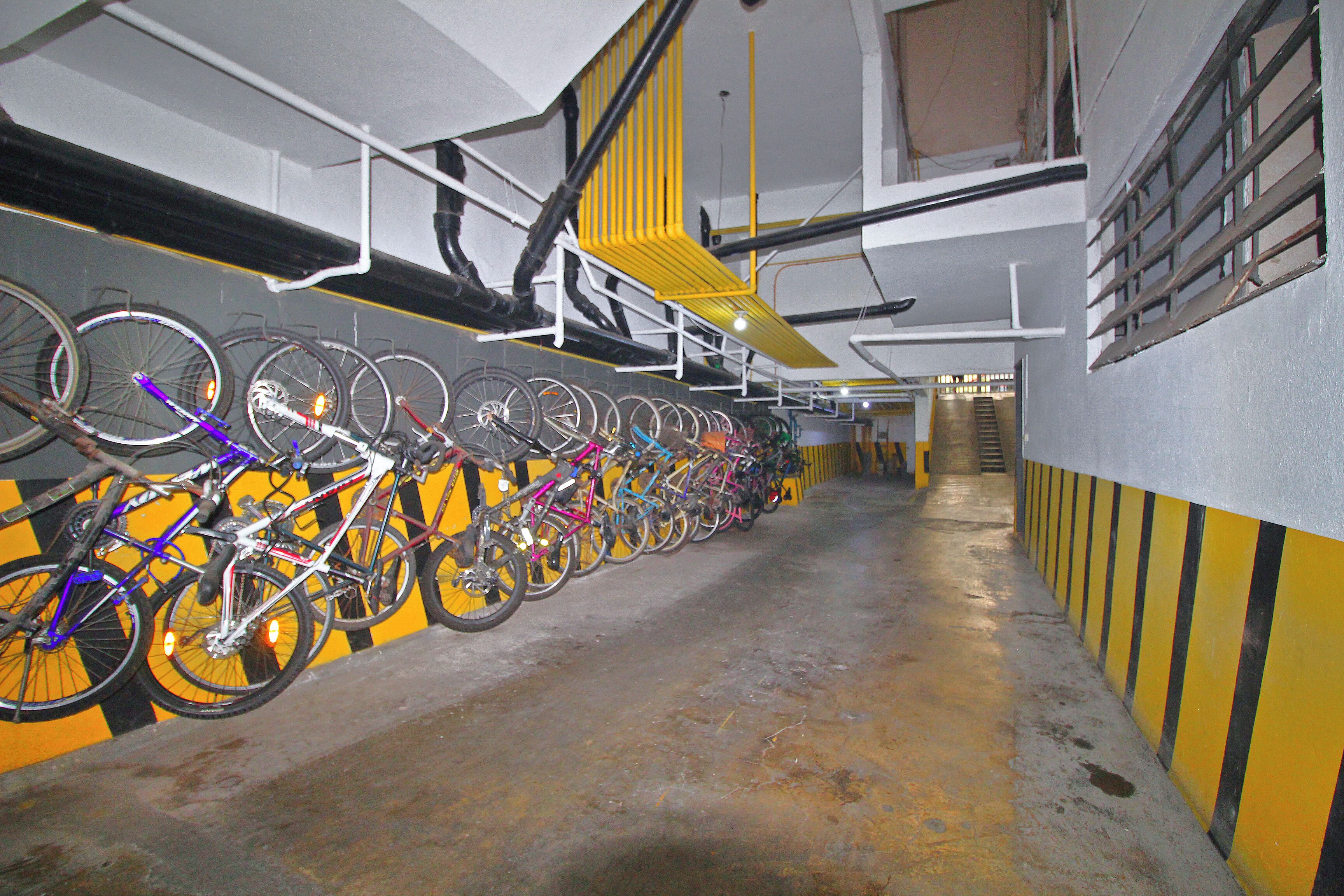 A row of bicycles parked in a covered area with a yellow and black striped wall.
