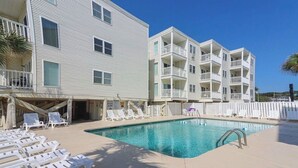 Une piscine avec des chaises longues, un bâtiment doté de balcons et un ciel dégagé.
