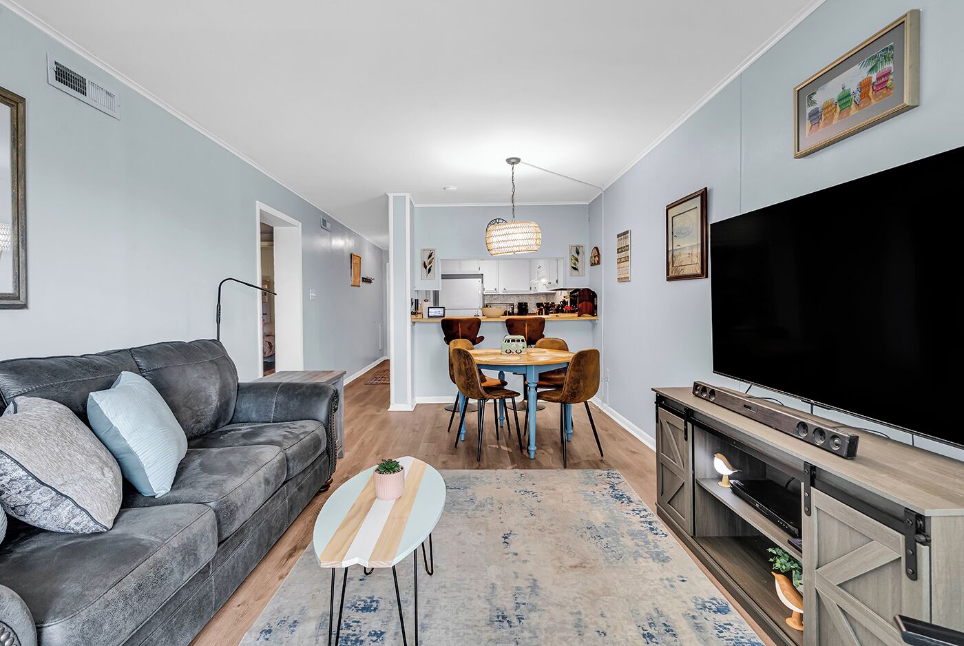 En moderne stue med en grå sofa, et fjernsyn og et spiseområde med et bord og stole.