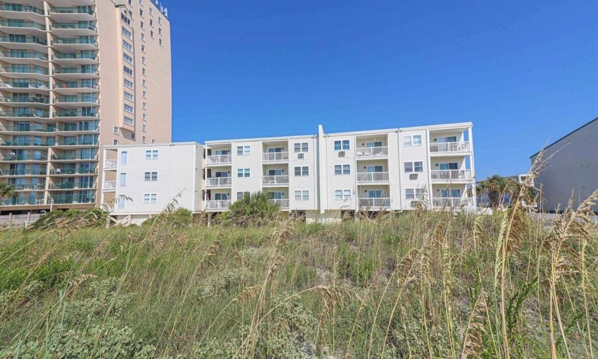 Un edificio de varios pisos con balcones, techo plano y cielo azul despejado.
