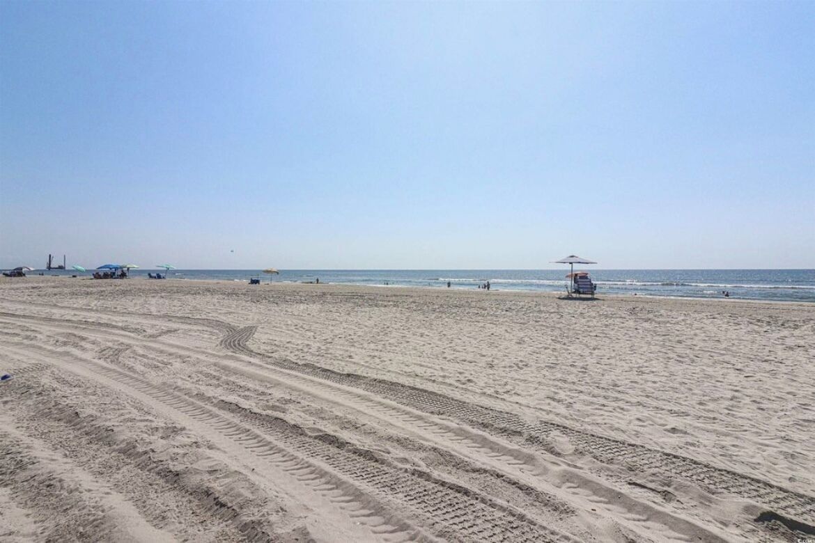 Une plage où l’on voit des traces de pneus, un poste de surveillance pour les sauveteurs et quelques chaises de plage.