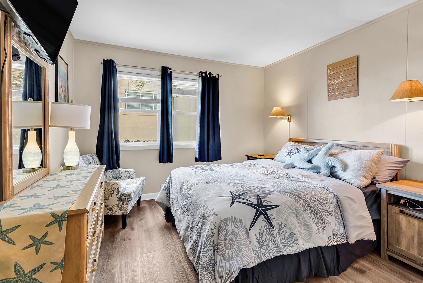 A bedroom with a bed, bedside tables, a nightstand, a dresser, a mirror, curtains, and a window.