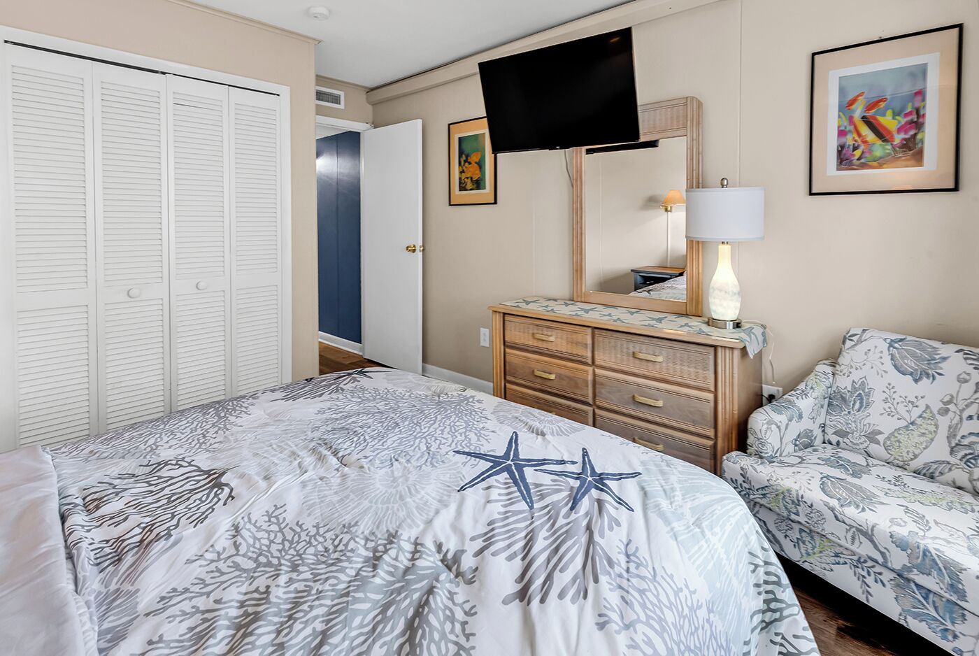 Une chambre à coucher avec un lit, une commode, un téléviseur et un tableau.