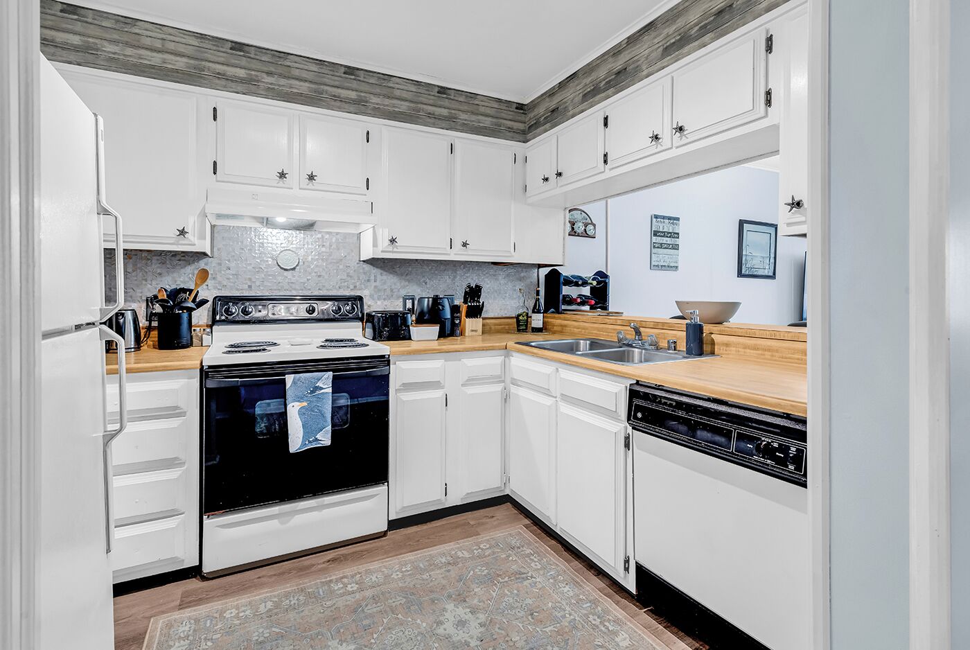 A kitchen with white cabinets, a stove, a dishwasher, and a wooden countertop.