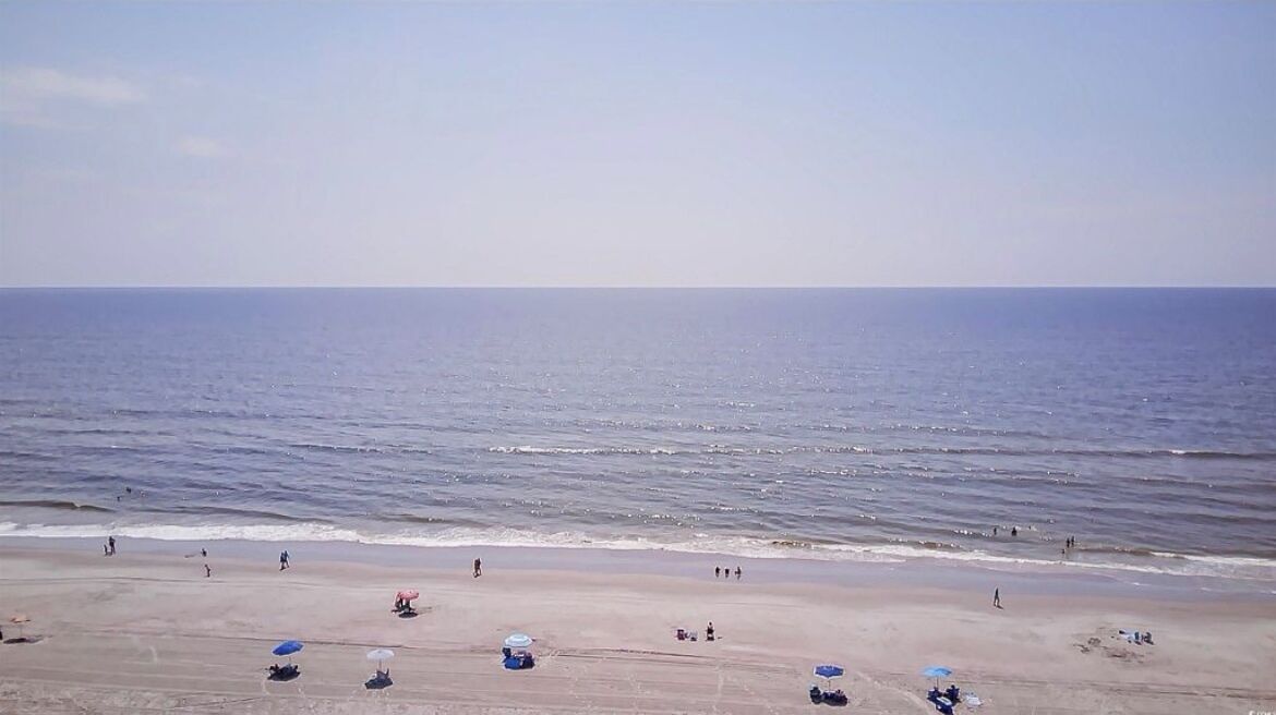 A beach with people, umbrellas, and a clear sky.