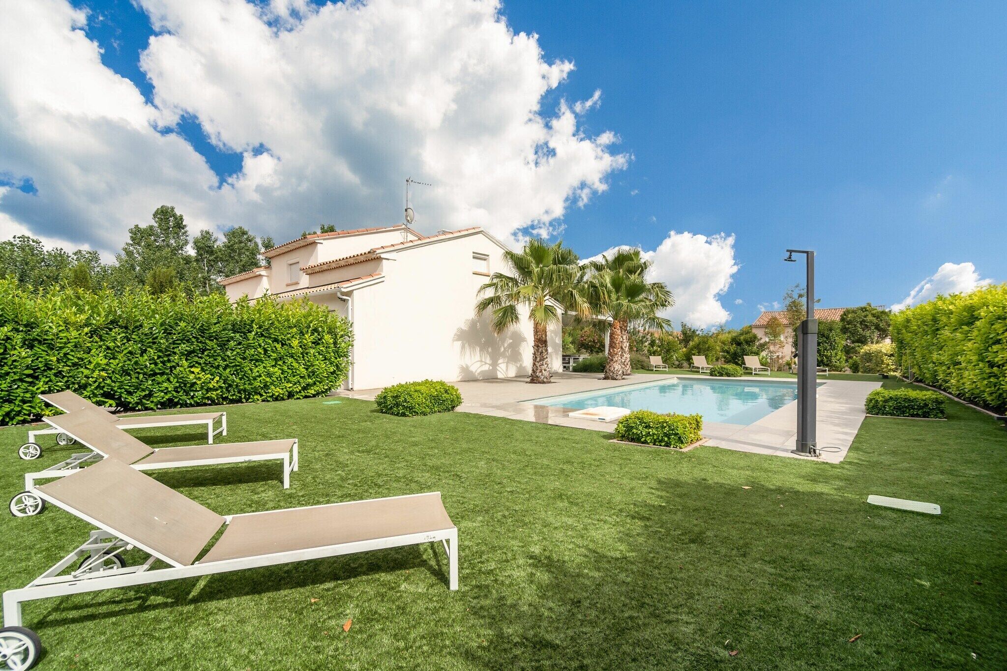 Un patio trasero con piscina, sillas de descanso, palmeras y un edificio blanco.