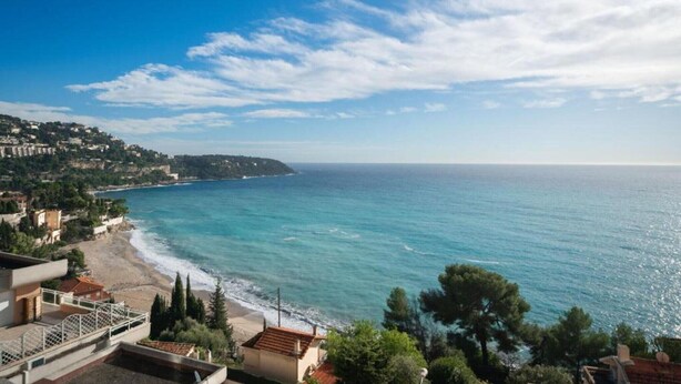A coastal view with a beach, ocean, and buildings in the background. - Villa w/ Palm Trees & Pool (Saint geniès de Fontedit)