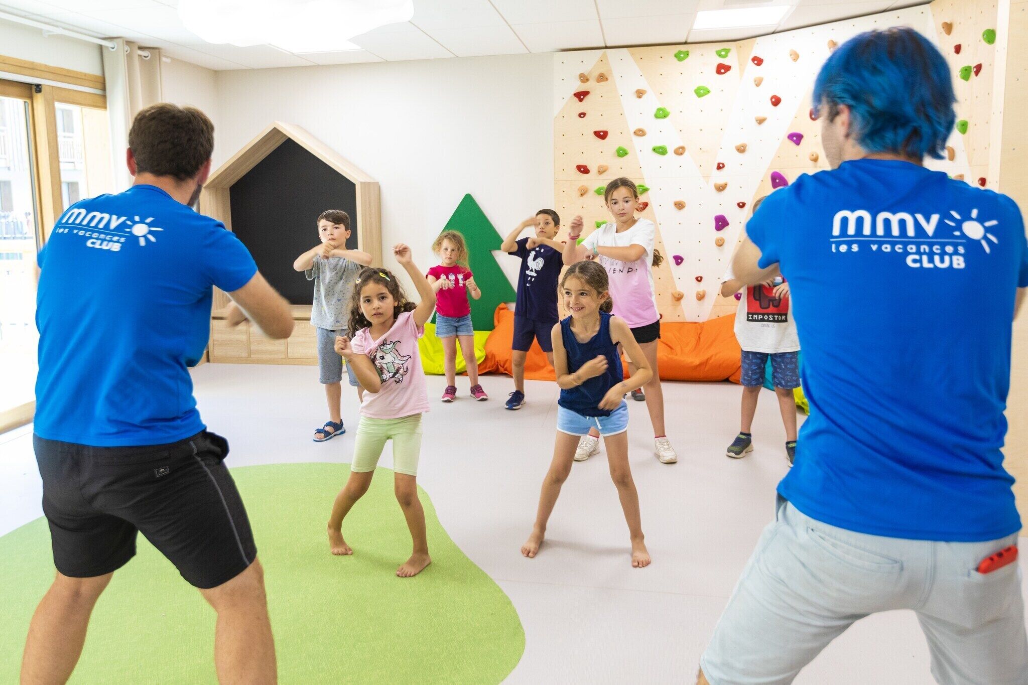 A group of children and adults in a climbing gym with climbing walls and padded flooring.