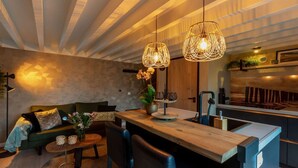 Une cuisine moderne avec un plan de travail en bois, un évier et une cuisinière encastrée. On y trouve également un coin repas avec une table et des chaises en bois, ainsi qu’un canapé avec des coussins.