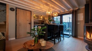 Un salon chaleureux avec une cheminée, un plafond en bois et un coin repas comprenant des chaises et une table.