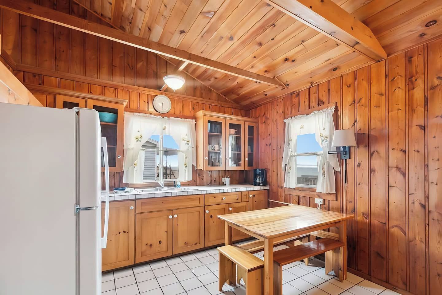 Interno di una baita in legno con angolo cottura, comprendente mobili, frigorifero, lavello e tavolo da pranzo.