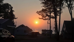 Une rue résidentielle bordée de maisons et de voitures garées, au coucher du soleil.